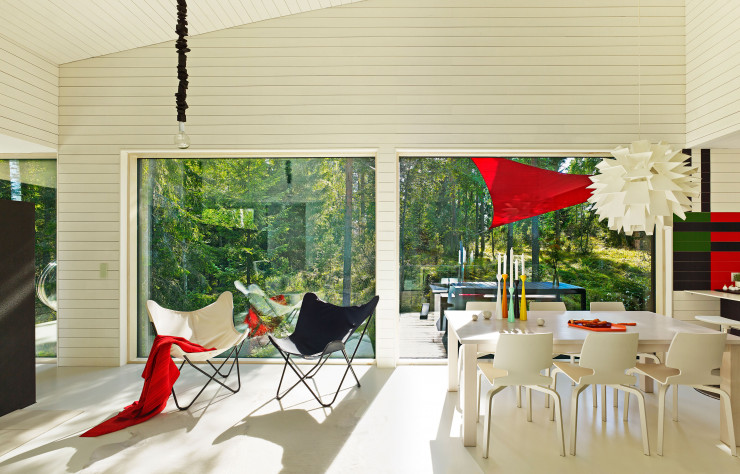 La blancheur des murs lambrissés et du sol en pierre du salon est ponctuée de touches colorées. Dans cet espace à vivre très lumineux, fauteuils Leppako (Varax), chaises de salle à manger HK001 de Harri Koskinen (Artek, 2006) et suspension blanche Norm