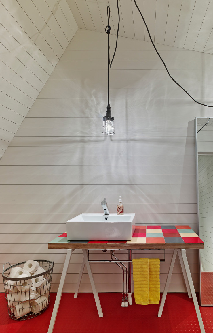 C’est un caoutchouc, rouge toujours, qui a été choisi pour recouvrir le sol de la salle de bains de l’étage. Le meuble sur lequel est posé le lavabo est un assemblage de piètement Hay et d’un plateau à damier coloré créé par Lasse Lehtinen.