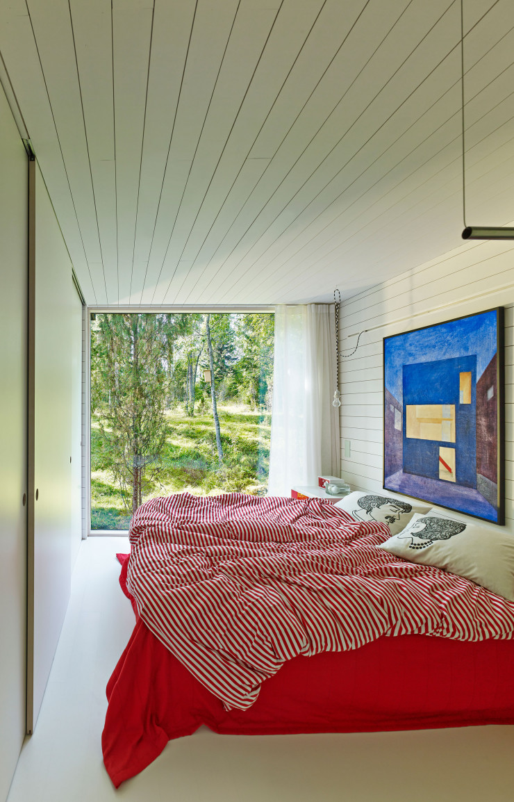 La grande baie vitrée de la chambre parentale offre, elle aussi, une vue imprenable sur le paysage. Au mur, un tableau de l’architecte Lasse Lehtinen.