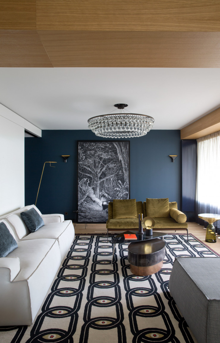 Sur le mur du fond, toile d’Aylin Langreuter (Dante). A gauche, canapé de Paola Navone avec pouf assorti (Baxter). Au fond, canapé d’Antonio Citterio (Flexform). Tapis « Eyes in Chains » de Federico Pepe (cc-tapis). Posés sur la table basse « Loren » de Draga & Aurel (Baxter), objets décoratifs « Peacok Candle Holder » de Dan Yeffet (Collection Particulière). Glissée dessous, table basse en céramique (Bitossi Ceramiche). A droite, table d’appoint « Bell Side » de Sebastian Herkner (ClassiCon). Lustre « Arctic Pear » (Ochre). Rideaux (Dedar). Peinture (Ressource).