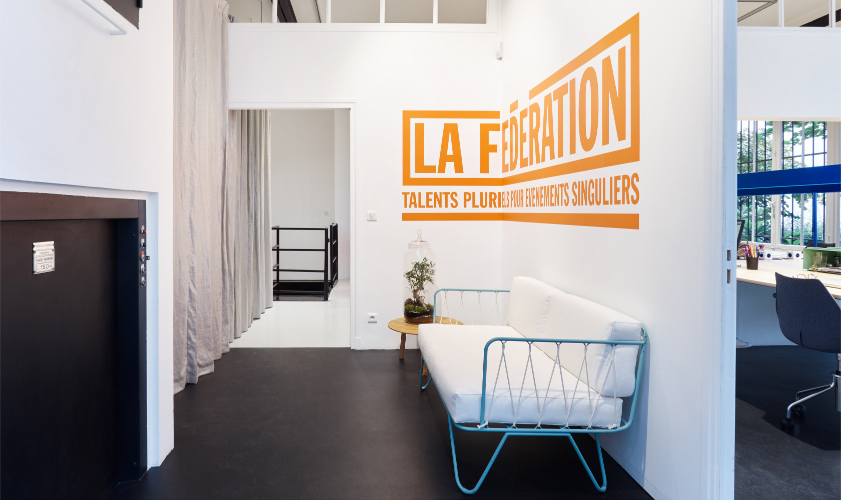 Dans l'entrée, un lit de jour et le logo de l'agence.