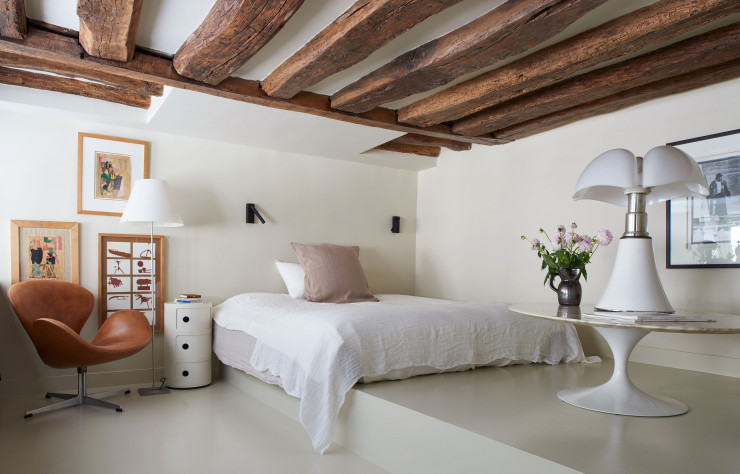 Dans l’entrée, la chambre d’amis, en mezzanine, est accessible depuis un escalier dérobé. Des collages d’Arthur Aeschbacher et une photo de Joseph Beuys cohabitent avec le fauteuil « Swan » d’Arne Jacobsen (Fritz Hansen), la lampe « Pipistrello » de Gae Aulenti (Martinelli Luce), la table basse « Tulip » d’Eero Saarinen (Knoll) et le meuble de rangement « Componibili » d’Anna Castelli Ferrieri (Kartell). Linge de lit Couleur Chanvre.