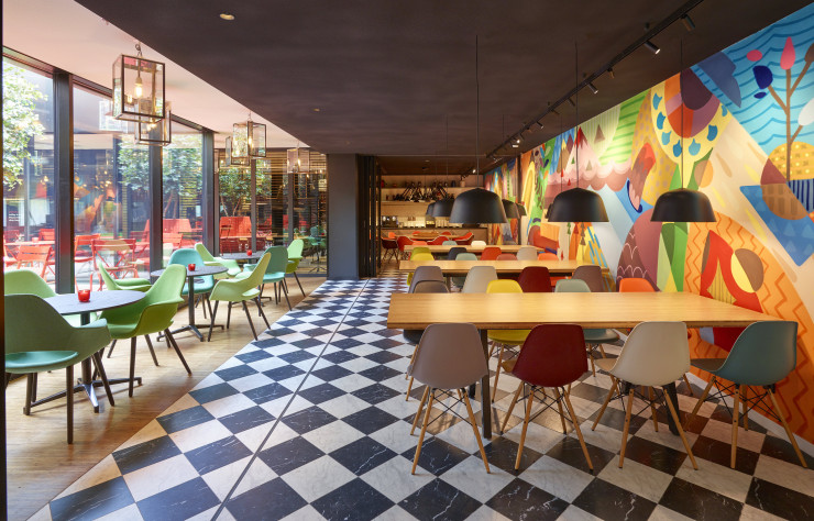 Accolées à une fresque réalisées sur-mesure, les tables profitent de la lumière naturelle apportée par l’atrium central.