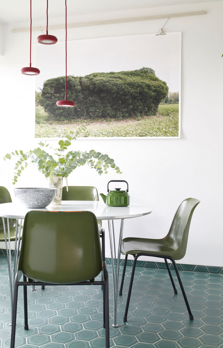 Idéal dans une cuisine, le carrelage d’origine a volontairement été conservé, conférant à cette pièce tout son cachet. Super Elliptical Table d’Arne Jacobsen (Fritz Hansen) entourée de chaises chinées. Photo imprimée sur papier d’art coton de Mathieu Karst. Suspension Hal rouge de Guillaume Delvigne (La Chance).