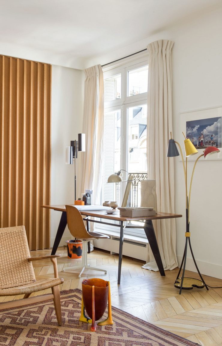 Charlotte Macaux Perelman a choisi une table de Jean Prouvé. Celle-ci a été transformée en bureau dans un coin du salon. Chaise du designer américain George Nelson. Lampadaire issu des puces de Saint-Ouen. Au premier plan, un vase en résine de Gaetano Pesce posé sur un tapis en paille marocain.