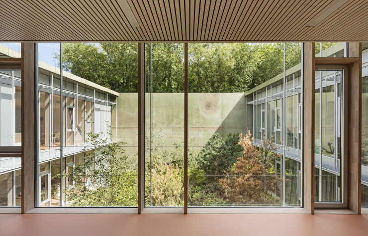 Succession de pleins et de vides, l’édifice englobe cinq jardins intérieurs qui prolongent le bois attenant, multipliant autant que possible les vues sur la nature verdoyante.