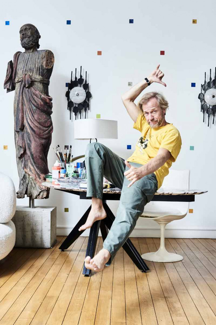 Le designer Hubert de Malherbe est assis sur un bureau dont le plateau est en marbre arabescato rosso et le piétement en acier (création Hubert de Malherbe). Au mur, deux appliques de style brutaliste en métal dénichées au marché Paul Bert des Puces de Saint-Ouen (chez Emmanuel Renoult). La statue de saint Pierre date du XIXe siècle.