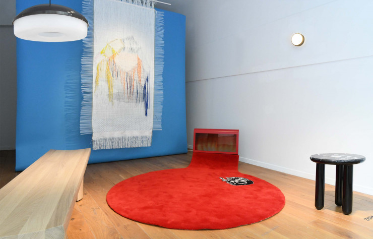 Au sol, tapis Sleeping Cat des Radi Designers. Banc Hakone, de Barber & Osgerby, éclairé par la suspension 233 (1958) de Gino Sarfatti (Arteluce). Table d’appoint Hymy Black, design Jaime Hayón. Sur fond bleu, toile tissée 8:15 AM, série « The Woven Movie », de Hella Jongerius.