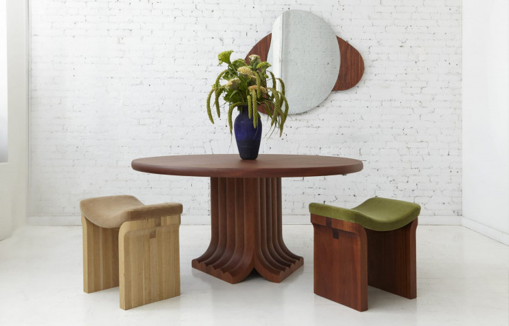 La table à manger Bole comporte un plateau arrondi placé au sommet d’une base de piédestal faite d’arcs en bois répétés (Colony).