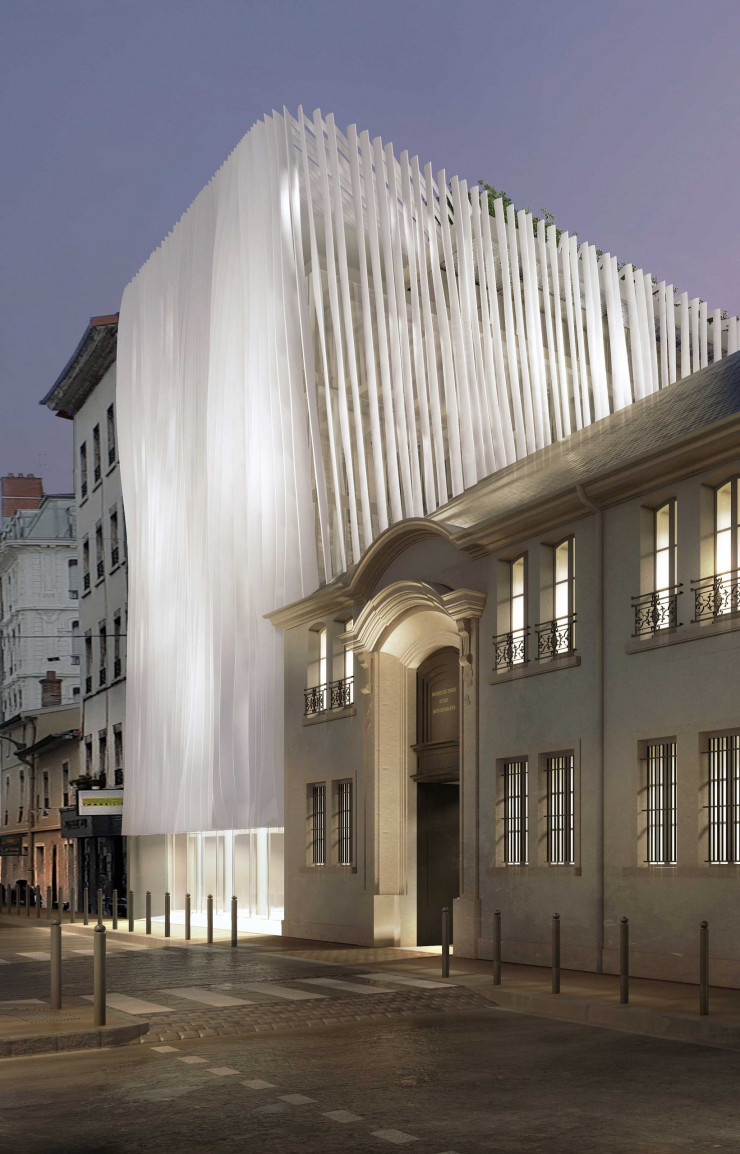 De nuit, l’entrée se fait spectaculaire avec son drapé de béton et de verre.