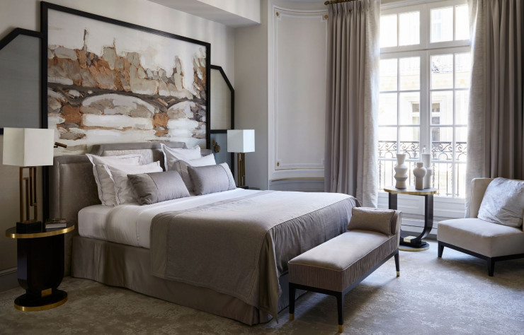 Chambre de l’Hôtel Elysia. Assorties aux nuances pastel des étoffes, les têtes de lit peintes par l’artiste évoquent le paysage impressionniste des toits parisiens, le jardin des Tuileries ou le pont des Arts.
