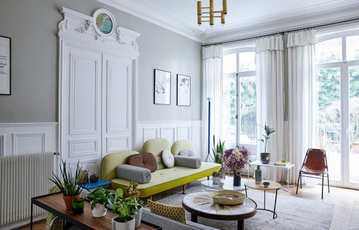Le salon lumineux et accueillant de chez Véronique et François qui donne sur un jardin à la végétation luxuriante. Les impostes au dessus des portes ont été comblés par des cartes d’écoles chinées dans le but d’animer ces éléments.