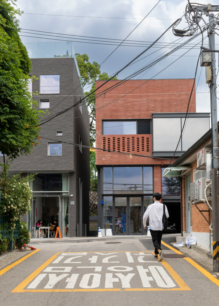 Au milieu des vieux hanok du quartier de Seochon, de très contemporains et chics condominiums fleurissent : attablée au café, en arrière-plan, c’est l’ancienne Miss (Canada), June Elizabeth Kang, qui déjeune à la fraîche. Au sol, les inscriptions indiquent qu’il s’agit d’un chemin sécurisé pour que les femmes puissent rentrer tranquillement chez elles – la mairie commence à se préoccuper des violences faites aux femmes dans l’espace public et privé.