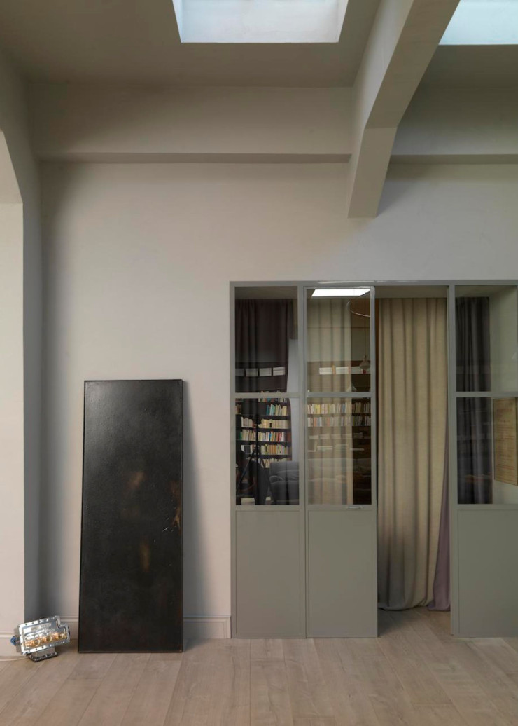 Pile et face, les portes vitrées séparant la chambre de la cuisine. Les lames du plancher en chêne pigmenté de blanc apportent chaleur et douceur. Des rideaux en lin assurent l’intimité. Posée au sol, peinture noire de la série « Tentativo di Esistenza » de Giovanni Manfredini.