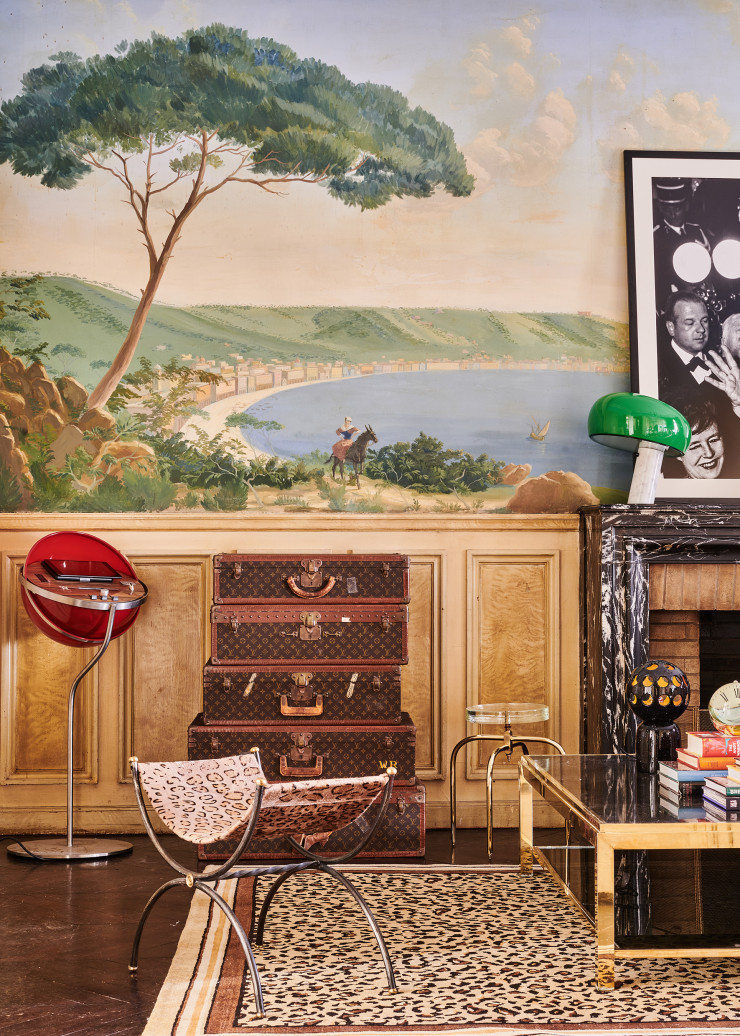 Des valises Vuitton reposent sagement sous un panoramique du peintre Guy Roisse, qui représente la baie de Naples, ville de naissance de Willy Rizzo. Table basse Flaminia ; à gauche, console HI-FI Galileo rouge ; photo d’Alfred Hitchcock au Festival de Cannes (toutes de Willy Rizzo). Sur la cheminée, lampe Snoopy en marbre, en métal et en verre, design Achille et Pier Giacomo Castiglioni (Flos). Dessous, tabouret Dorique en laiton poli, en or pâle et en verre (Mydriaz). Sur la table, luminaire noir ajouré en céramique, collection « Spacetrip » (Villa Arev).