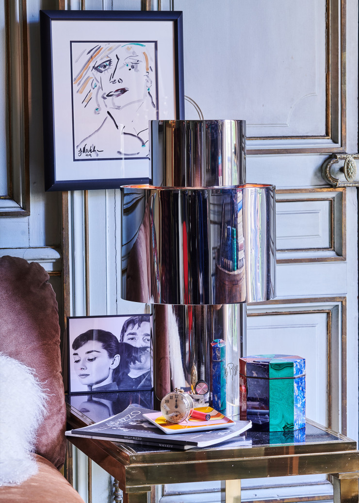 / De l’autre côté du canapé, sur une autre table Flaminia, la lampe Love dans sa version ronde en acier, intérieur cuivre. Parmi les souvenirs personnels, une photo de Willy Rizzo avec Audrey Hepburn et un dessin de Jack Nicholson représentant sa propre compagne, l’actrice Rebecca Broussard, mère de deux de ses enfants. Sous le réveil, plateau Riviera Arch en céramique (Octaevo).