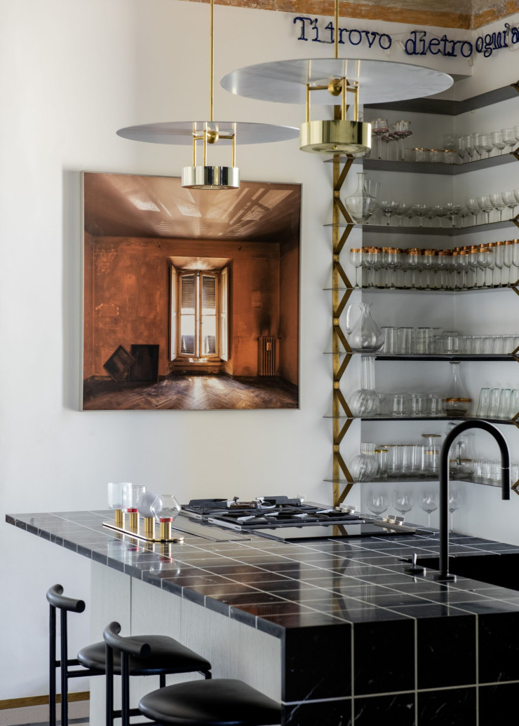 Comptoir de cuisine encastré avec côté et dessus en marbre noir gravé d’un dessin quadrillé Alfa Marmi. Cuisinière Gaggenau et robinetterie Zucchetti. Bougies et vases Paola C. Tabourets en acier Tokyo, design Rodney Kinsman (Bieffeplast). Suspensions, design Hans-Agne Jakobsson. Étagère sur mesure en laiton et en métal. Photographie signée Luciano Romano.
