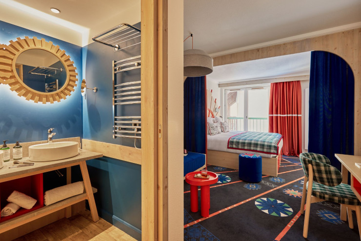 Vue d’une chambre Supérieure Junior Famille, prévue pour deux adultes et un enfant de moins de 11 ans, orientée pour bénéficier au maximum de l’ensoleillement. Sa moquette reproduit des motifs inspirés de la signalétique des pistes de ski.