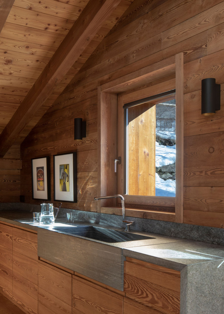 Dans la cuisine du chalet, le bois de mélèze omniprésent contraste avec la pierre de Courtil utilisée pour le plan de travail et l’évier.