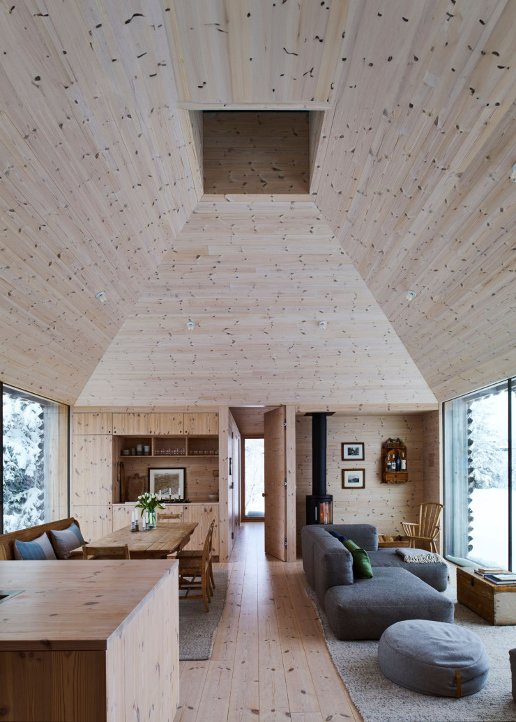 Dans le séjour, les propriétaires ont opté pour un intérieur intégralement recouvert de pin noueux, avec de spectaculaires hauts plafonds typiques des fermes de montagne norvégiennes, surmontés d’un puits de lumière pour accentuer l’espace et le volume des pièces. La menuiserie et les rangements ont été réalisés sur mesure. Au fond à droite, étagère suspendue acquise à une vente aux enchères chez Blomqvist. À côté du poêle à bois HWAM, fauteuil norvégien à barreaux ancien acheté aux enchères chez Antikkvarehuset. Coffre chiné, détourné en table basse. Sofa Mags (Hay), pouf Mochi (Hübsch). Coussins Røros Tweed.